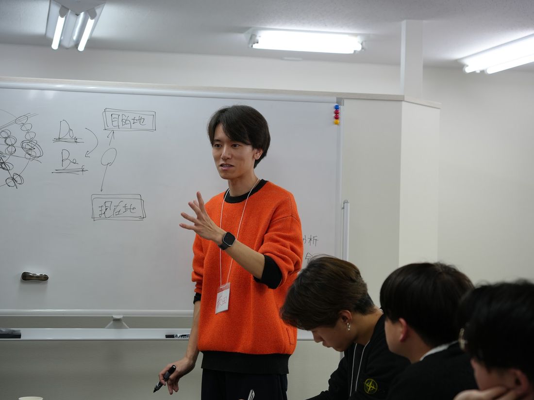 ホワイトボードの前で学生に解説するスタッフ